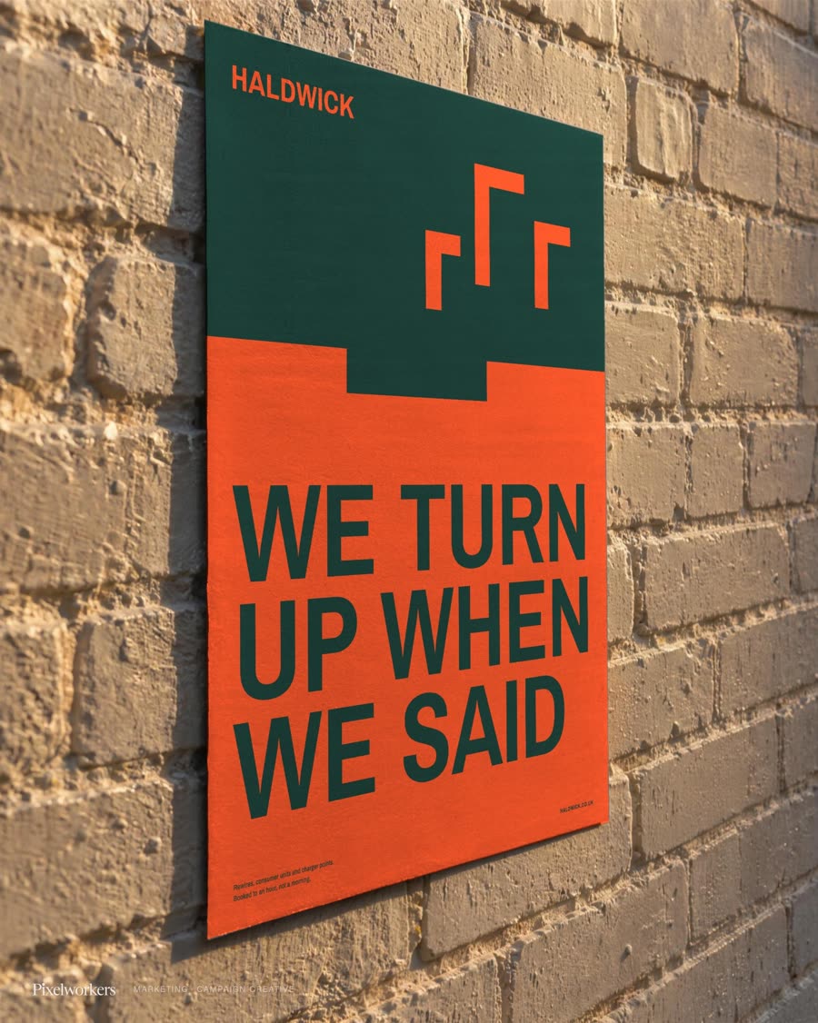 An orange and dark green poster pasted flat on a sunlit brick wall seen at a steep angle.
